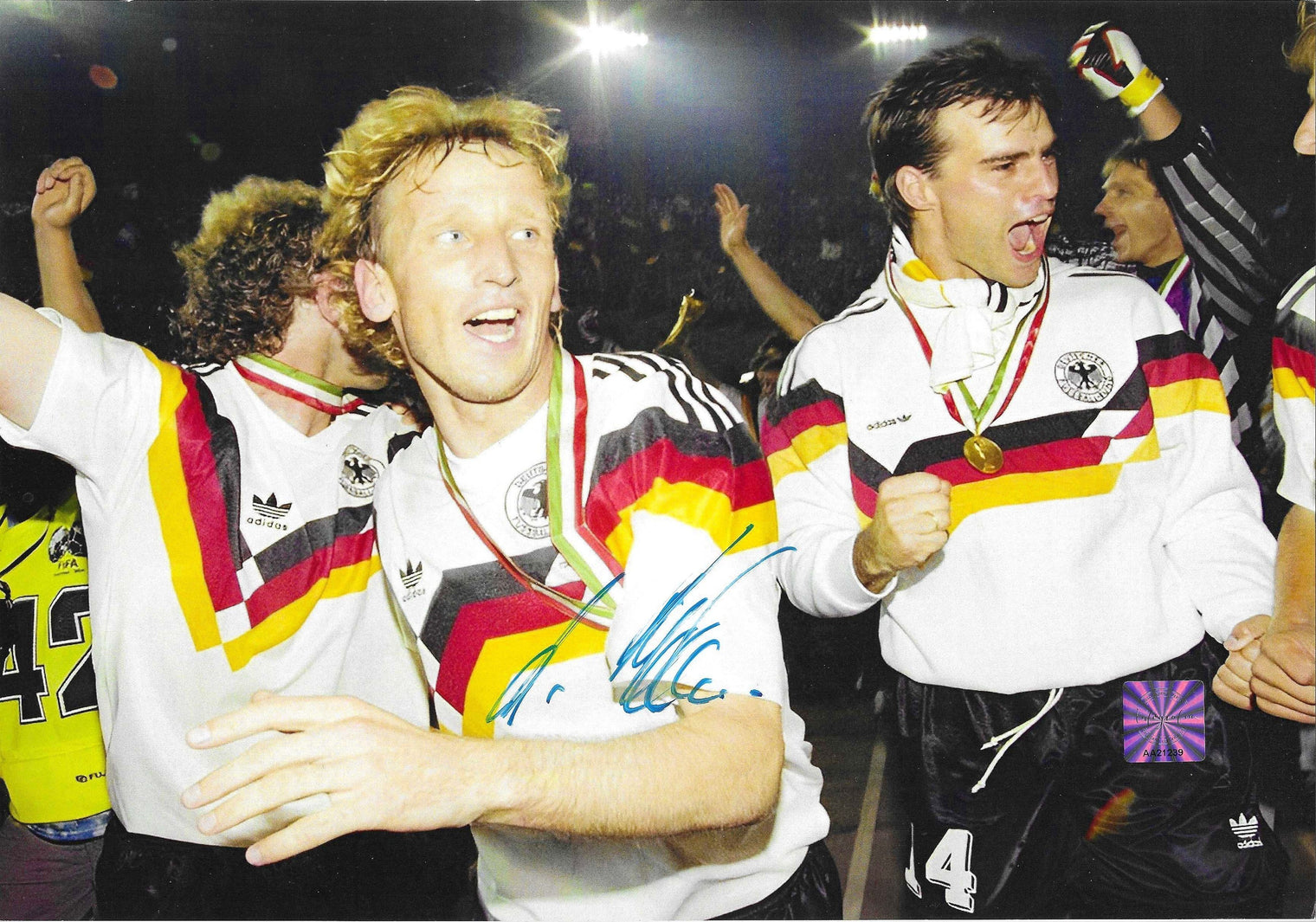 Fotografia autografata Andreas Brehme festa post vittoria Mondiali Italia 1990 tuta Adidas Germania medaglia oro al collo compagni squadra esultanza ologramma sicurezza Associazione Autografia – autografo originale pennarello blu al centro – 29,3x20,5 cm – condizioni Excellent