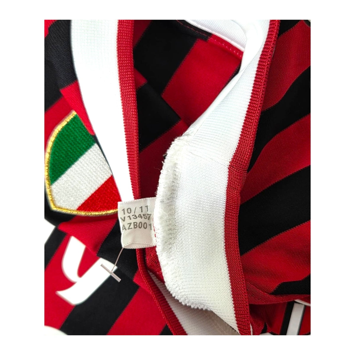 Cartellino Adidas con codice V13457 e data 10/11 accanto allo scudetto della maglia Milan 2011/12