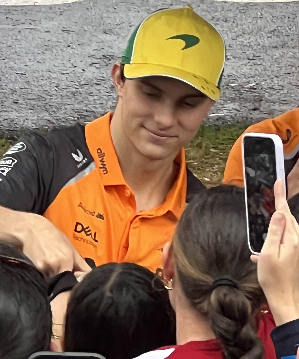 Oscar Piastri pilota McLaren Formula 1 firma autografi ai tifosi durante Gran Premio, con cappellino McLaren edizione Australia e polo papaya stagione 2025
