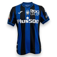 Fronte maglia Atalanta BC Home 2022-23 Store – Joma – sponsor Plus500 Radici Group – stemma Atalanta – patch Coppa Italia Serie A