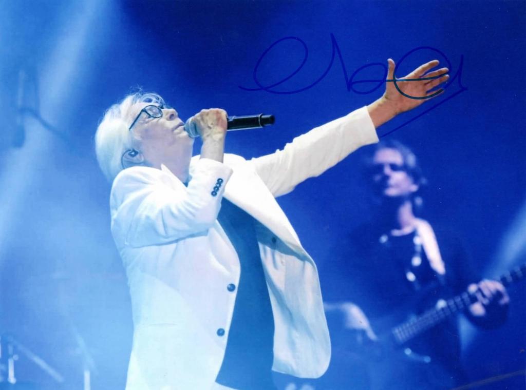 Fotografia autografata Nino D'Angelo al concerto – abito bianco con microfono – autografo originale pennarello blu in alto a destra – luci blu sul palco – condizioni Excellent