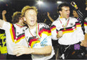 Fotografia autografata Andreas Brehme festa post vittoria Mondiali Italia 1990 tuta Adidas Germania medaglia oro al collo compagni squadra esultanza ologramma sicurezza Associazione Autografia – autografo originale pennarello blu al centro – 29,3x20,5 cm – condizioni Excellent