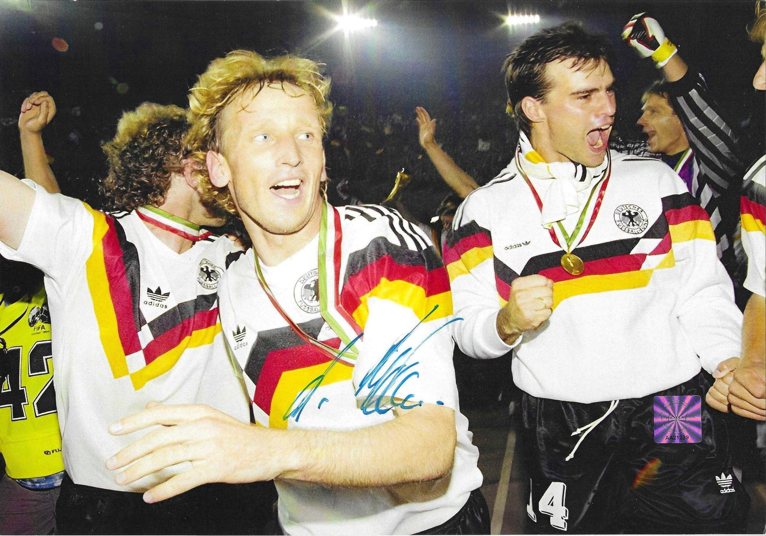 Fotografia autografata Andreas Brehme festa post vittoria Mondiali Italia 1990 tuta Adidas Germania medaglia oro al collo compagni squadra esultanza ologramma sicurezza Associazione Autografia – autografo originale pennarello blu al centro – 29,3x20,5 cm – condizioni Excellent