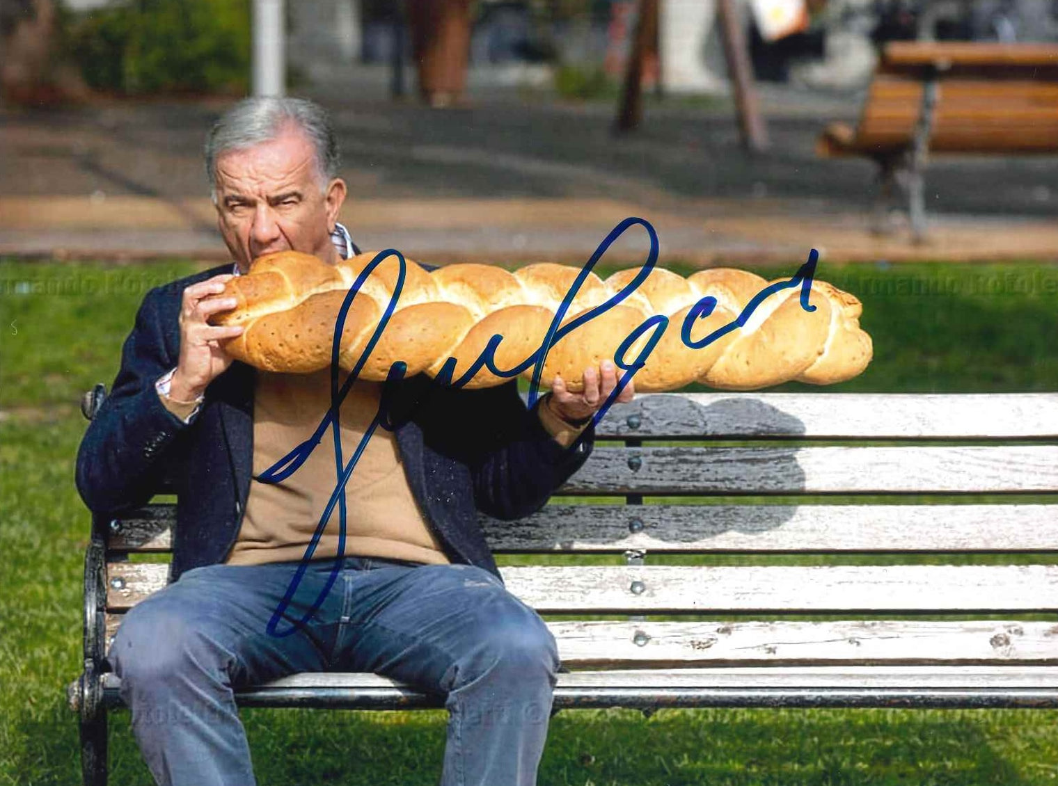 Fotografia autografata Gene Gnocchi comico su panchina mentre addenta una treccia di pane – gag surreale foto Armando Rotoletti – autografo originale pennarello blu