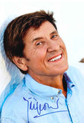 Fotografia autografata Gianni Morandi ritratto sorridente a colori camicia azzurra appoggiato a muretto bianco cantante italiano leggenda della musica – autografo originale pennarello blu – 30x20 cm