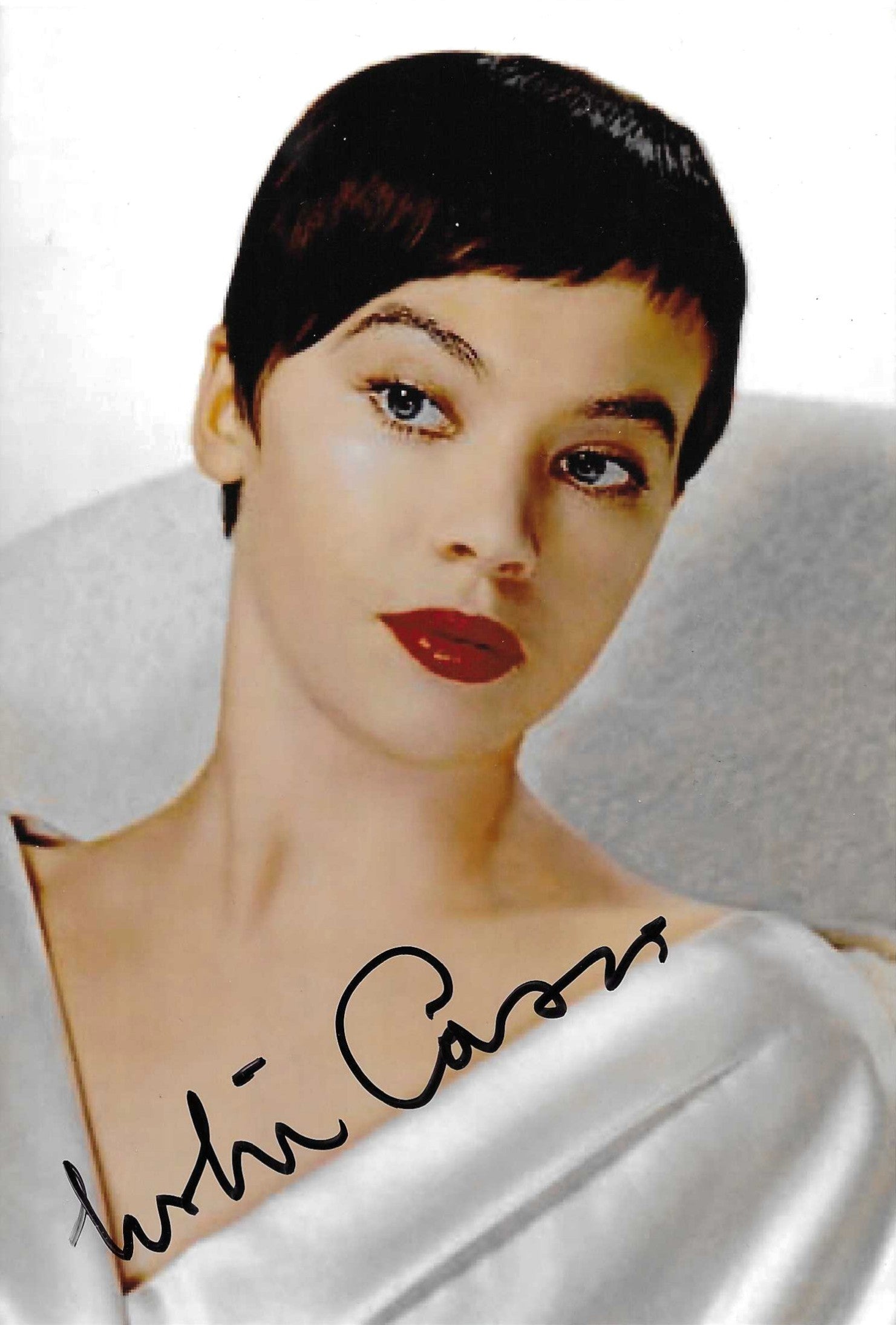 Fotografia autografata Leslie Caron ritratto a colori capelli corti scuri caschetto sguardo intenso labbra rosse abito bianco satinato Hollywood anni 50 – autografo originale pennarello nero in basso ampio – 18,8x12,2 cm – condizioni Excellent