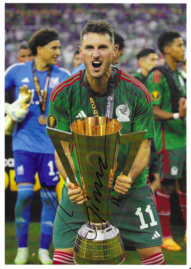 Fotografia autografata Santiago Giménez solleva trofeo CONCACAF Gold Cup urlo di gioia maglia Nazionale Messico verde Adidas numero 11 Ochoa sullo sfondo medaglia oro – autografo originale pennarello nero al centro – 30x21 cm – condizioni Excellent