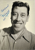 Fotografia con dedica datata 1955 autografata Fernandel ritratto bianco e nero sorridente camicia quadretti sfondo chiaro – dedica originale inchiostro blu cordialement Fernandel 1955 in alto a sinistra – 12,8x18 cm – condizioni Excellent