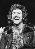 Fotografia con dedica autografata Gigi Proietti primo piano scena teatrale bianco e nero in costume ricco pizzi capelli ricci bocca aperta espressione di riso sfondo nero – dedica autografa originale pennarello scuro al centro – 15x10,5 cm – condizioni Excellent