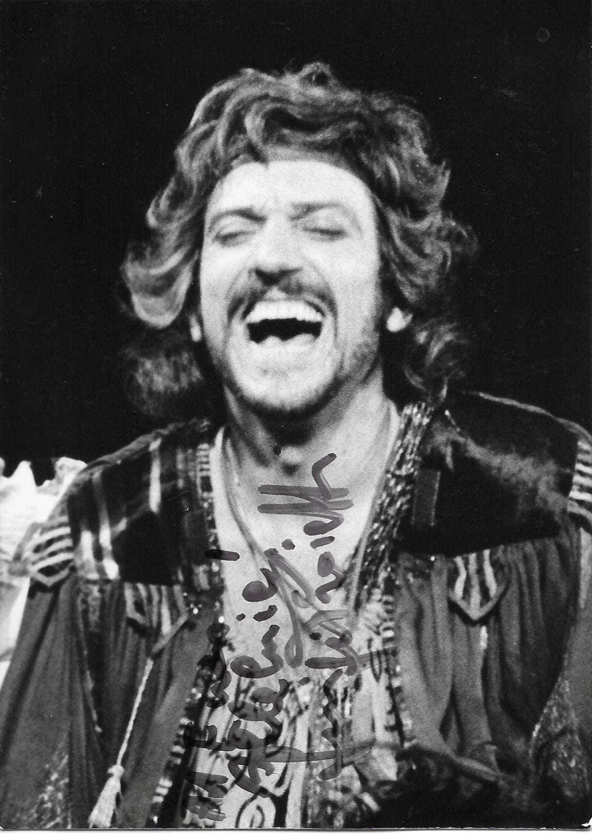 Fotografia con dedica autografata Gigi Proietti primo piano scena teatrale bianco e nero in costume ricco pizzi capelli ricci bocca aperta espressione di riso sfondo nero – dedica autografa originale pennarello scuro al centro – 15x10,5 cm – condizioni Excellent