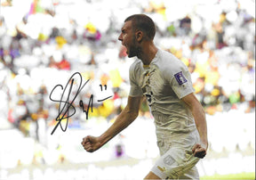 Fotografia autografata Strahinja Pavlovic esultanza urlo primo piano profilo maglia bianca Puma Serbia patch FIFA Qatar 2022 pugno chiuso – autografo originale pennarello nero con numero 11 – 29,7x21 cm – condizioni Excellent