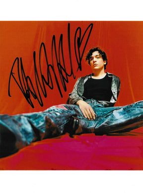 Fotografia autografata Tananai ritratto a colori posa sdraiata sfondo arancio rosso – firma originale pennarello nero – 20x15 cm – condizioni Excellent