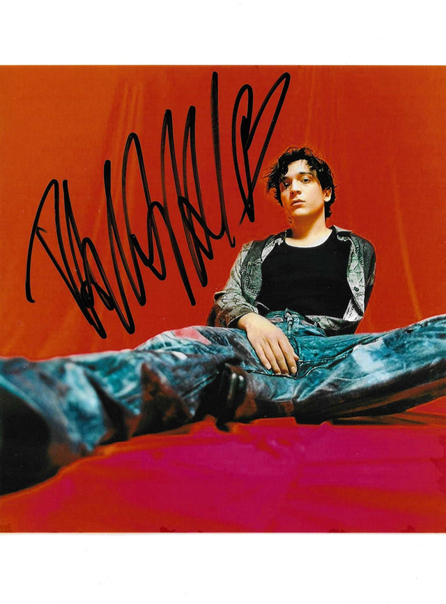 Fotografia autografata Tananai ritratto a colori posa sdraiata sfondo arancio rosso – firma originale pennarello nero – 20x15 cm – condizioni Excellent